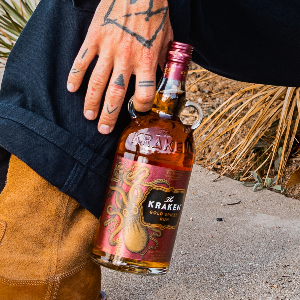 Lifestyle image of model hand holding a bottle of The Kraken Gold Spiced Rum