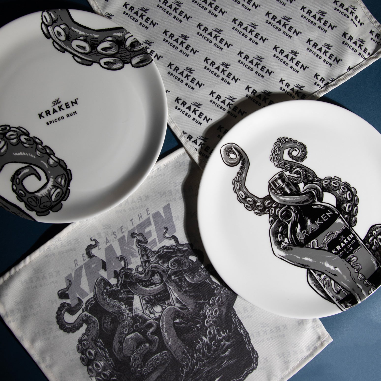 Items Included: Two ceramic plates and two cloth napkin.
Design Theme: Each item features black-and-white illustrations of octopus tentacles, consistent with Kraken Rum's branding.
Branding: The plates prominently display the "KRAKEN" logo and the phrase "SPICED RUM," reinforcing the product association.
Packaging: The items are presented in a sleek black box, suggesting a premium or gift set presentation.