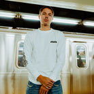 The image depicts a person standing on a subway platform in an urban setting wearing the Artist of the Abyss long sleeve.