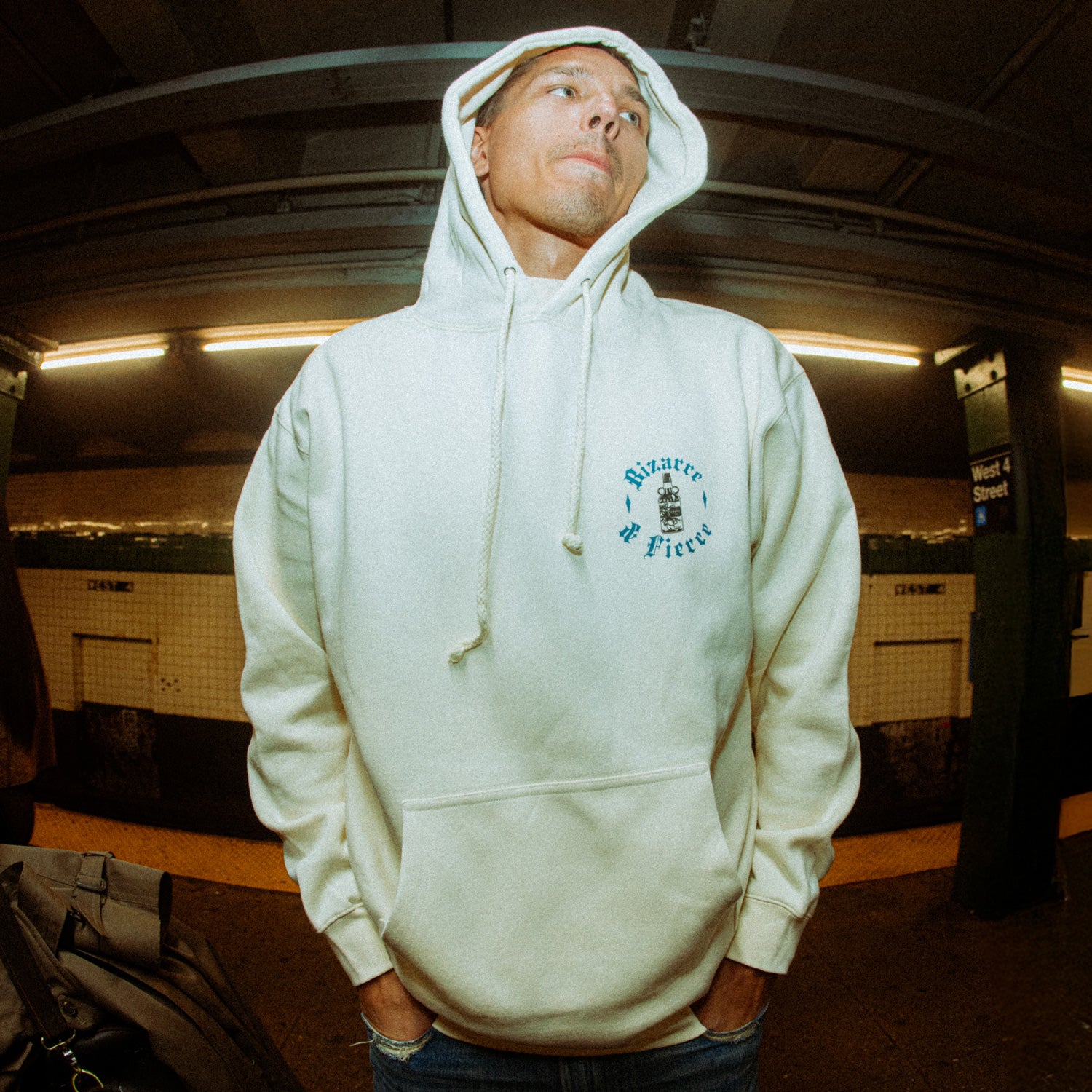 The image depicts a person wearing a white hoodie with a graphic design on the left chest area that reads "Bizarre & Fierce", standing in a subway station.