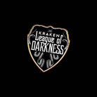 Pin resembling a shield with the text: "The Kraken League of Darkness," with a black background, white text, and a gold border.
