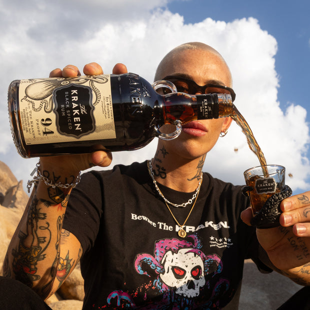 A lifestyle image of a model pouring Kraken Black Spiced Rum into the kraken shot glass outdoors.